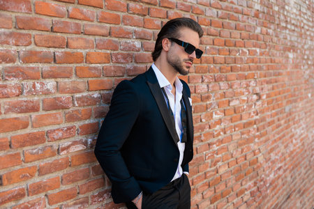 side view of elegant fashion man in suit with sunglasses posing with hands in pockets outdoors in a medieval city from Romaniaの写真素材
