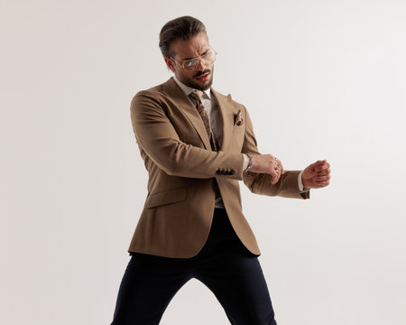 cool fashion man with glasses holding arms in fashion pose and looking to side in front of grey backgroundの写真素材
