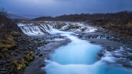 Bruarfoss waterfall on a cold and dark day flowing into a beautiful blue and milky riverの写真素材