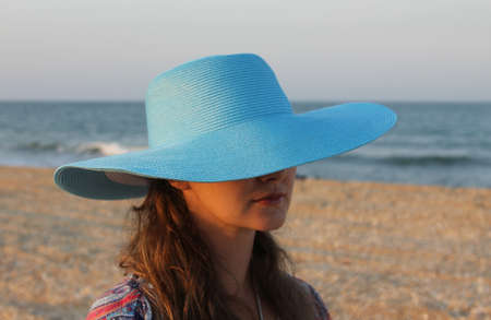 Young woman girl in blue wet hat on the sea sand coastline hiding her face. Golden hour. windy weather.の写真素材