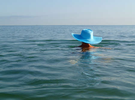 Young woman girl in blue hat swimming in the sea ocean. Sunny weather clear sky reflections.の写真素材