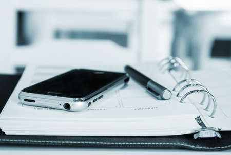 Mobile phone and pen on notebookの写真素材