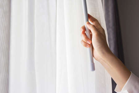 Young woman opening curtains in bedroomの写真素材