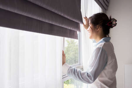 Young woman opening curtains in bedroomの写真素材