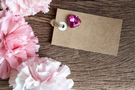 Blank paper tag with carnation flowers on wooden backgroundの写真素材