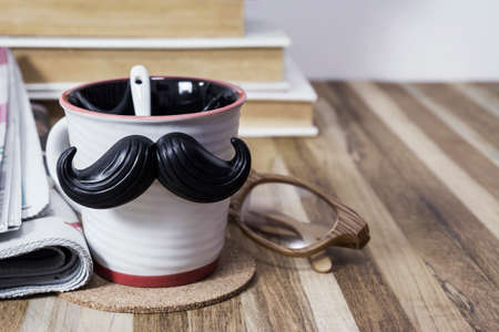 Cup with mustache on wooden table for fathers day conceptの写真素材