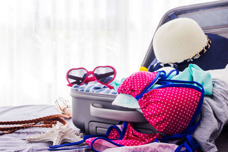 Pink bikini and clothes in suitcase on the bedの写真素材