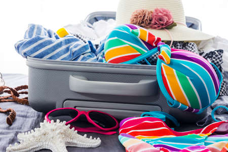 Colorful bikini and clothes in luggage on the bedの写真素材