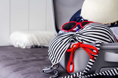 Colorful bikini and clothes in luggage on the bedの写真素材