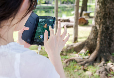BANGKOK, THAILAND - September 10, 2016: Young woman playing Pokemon Go game in public park. Pokemon...