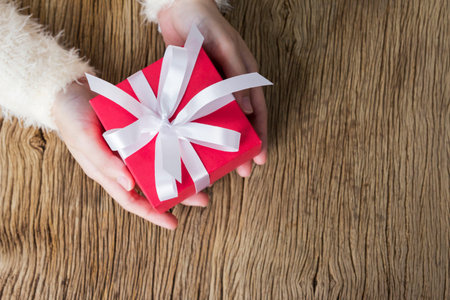 Young woman hands holding gift box on wooden tableの写真素材