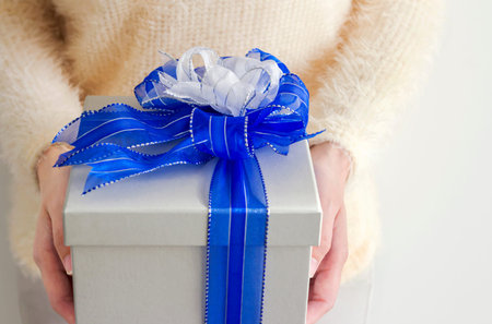 Young woman hands holding silver gift box with blue and white ribbon