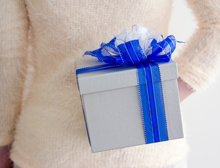 Young woman hiding silver gift box behind her backの写真素材