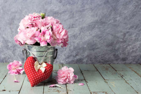 Red heart and pink carnation flowers in zinc bucket on old woodの写真素材