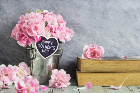 Pink carnation flowers in zinc bucket and old book on table wood