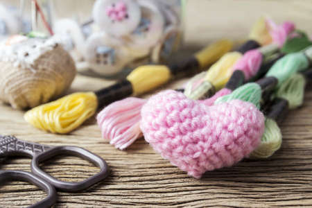 Pink heart knitting wool and sewing threads for embroidery on old wood tableの写真素材