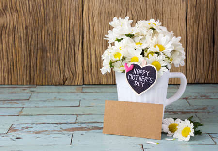 Happy mother's day on wood heart and blank brown paper tag and fresh daisies in white cupの写真素材