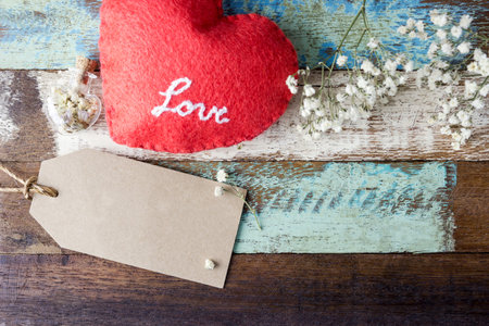 Love concept of blank brown paper tag with red heart and flowers on old wood for valentines day and weddingの写真素材