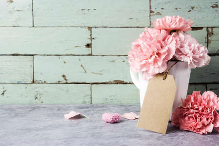 Pink carnation flower in white cup with blank brown paper tag and heartの写真素材