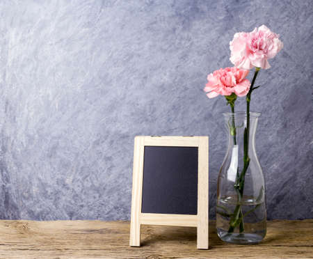 Mothers day concept of pink carnation flower in clear bottle and blank chalkboard on old wood with copy spaceの写真素材