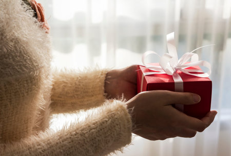 Young woman hands holding red gift box with white ribbon for christmas and new year and other...