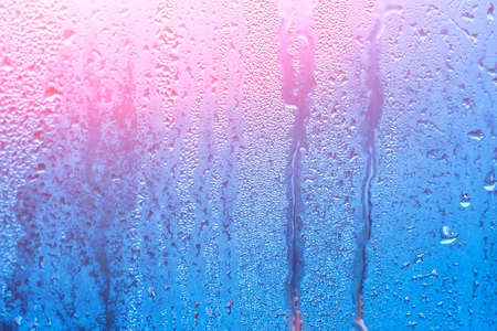 Window with condensate or steam after heavy rain, large texture or background with glare of lightの写真素材