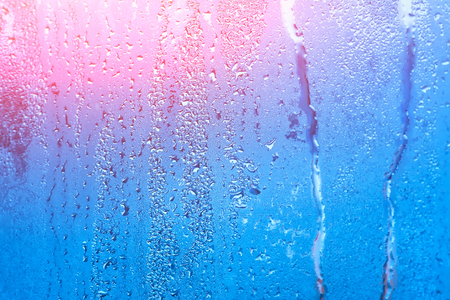 Window with condensate or steam after heavy rain, large texture or background with glare of lightの写真素材
