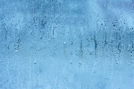Frozen glass of the window from the inside of the room. Background in a cool tone with a texture of dripping water dropsの写真素材