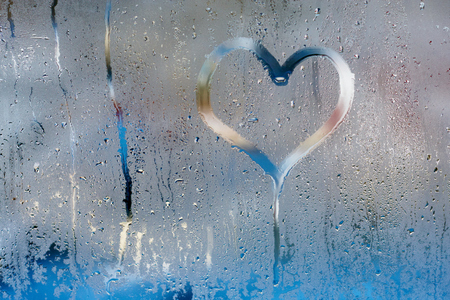 Hand draw a heart and drops of water on the glass. Condensation and raindrops on the window, shallow depth of fieldの写真素材