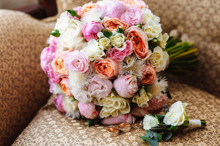 Beautiful wedding bouquet, two gold rings, boutonniere, lying on the armchair, wedding day. Important holiday accessoriesの写真素材