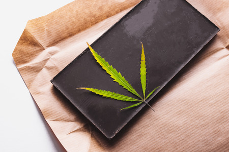 Marijuana leaf with edible dark chocolate block and cannabis brownie with ganja top view isolated on white backgroundの写真素材