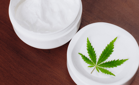 Jar of hemp white lotion. Detail of cannabis cream with marijuana leaf - cannabis topicals concept. Cream from biological and ecological plants of hemp vegetable pharmaceutical oil CBDの写真素材