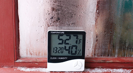 Electronic clock, calendar, thermometer, and hygrometer, against the background of condensation on...