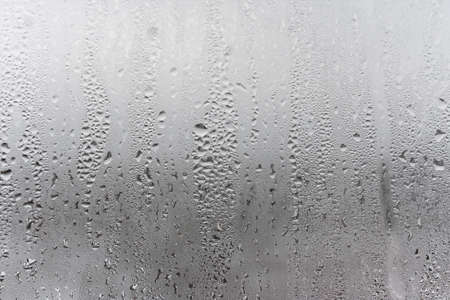 Natural drops of water flow down the glass, high humidity in the room, condensation on the glass window. Neutral colors. Excellent background with condensation drops texture. Horizontal orientation of the photoの写真素材