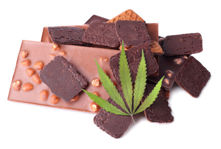 Green cannabis or marijuana leaf on chocolate bars and biscuits with chocolate on white isolated background containing CBD cannabis. Flat lay.の写真素材