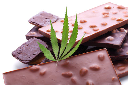 Chocolate with marijuana extract, chocolate biscuits with CBD content. Entertainment drugs concept. Chocolate bars with nuts and CBD cannabis content, green hemp leaf on white isolated background.の写真素材