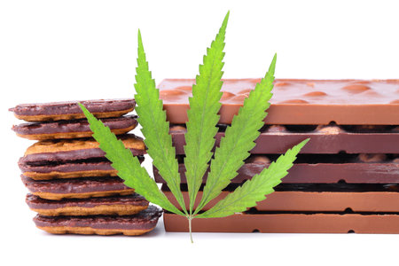 Chocolate with marijuana extract, chocolate biscuits with CBD content. Entertainment drugs concept. Chocolate bars with nuts and CBD cannabis content, green hemp leaf on white isolated background.の写真素材