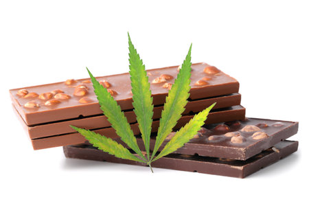 Two bars of black and three milk chocolate and a green hemp leaf on a white isolated background. Chocolate with marijuana extract. Entertainment drug conceptの写真素材