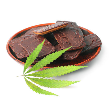 Chocolate chip cookie on saucer marijuana dessert with green hemp leaf on white isolated white backgroundの写真素材