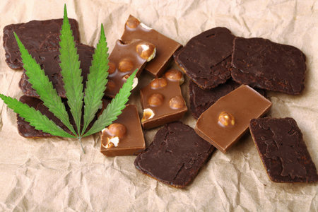 Pieces of delicious chocolate and cookies on the background of wrapping paper with a green hemp leaf. Cannabis Leaf Vegan Chocolate with CBD Supplement and Green Marijuana Leavesの写真素材
