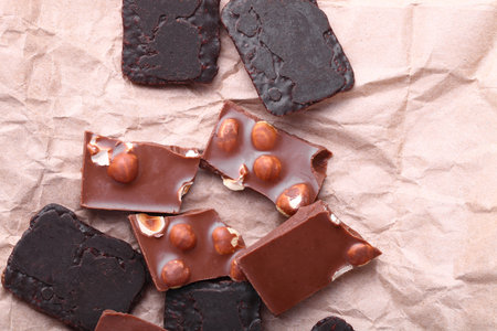 Pieces of chocolate with nuts and chocolate chip cookies close-up on wrapping paper background flat layの写真素材