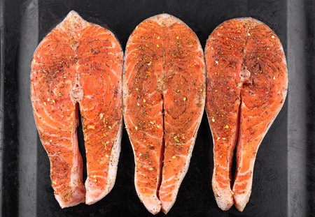 Preparation for cooking red salmon fish steaks with spices on a black tray on a white isolated background, top viewの写真素材