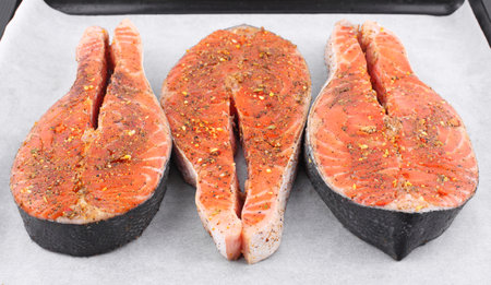 Red salmon fish steak in spices on white parchment paperの写真素材