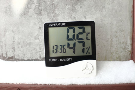 Digital thermometer on a window with snow on the background of frozen glass. Electronic thermometer and hygrometer for temperature and humidity controlの写真素材