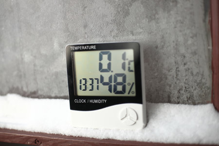 Digital thermometer on a window with snow on the background of frozen glass. Electronic thermometer and hygrometer for temperature and humidity controlの写真素材