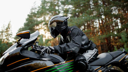 Motorcyclist in a helmet and leather protective gear close-up looks straight, sitting on a fast sports motorcycleの写真素材