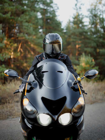 Motorcycle rider wearing a helmet looks straight ahead, headlights on. The concept of motorsport, speed and freedomの写真素材