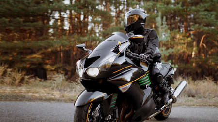 Handsome motorcyclist wear leather jacket and holding helmet on the roadの写真素材