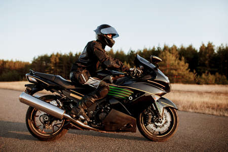 Man in black clothes riding a black classic American motorcycle in a road.の写真素材