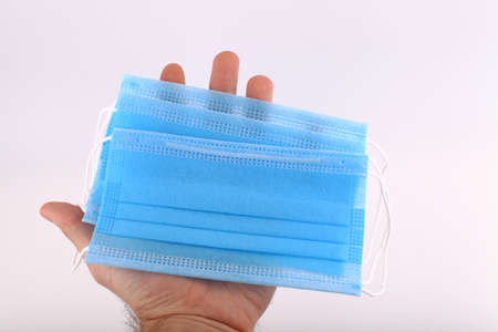 Hand holding a facial medical mask, white background, close up, copy space, banner. Flu epidemic, allergy season. The most sought after coronavirus, covid-19 protection productの写真素材